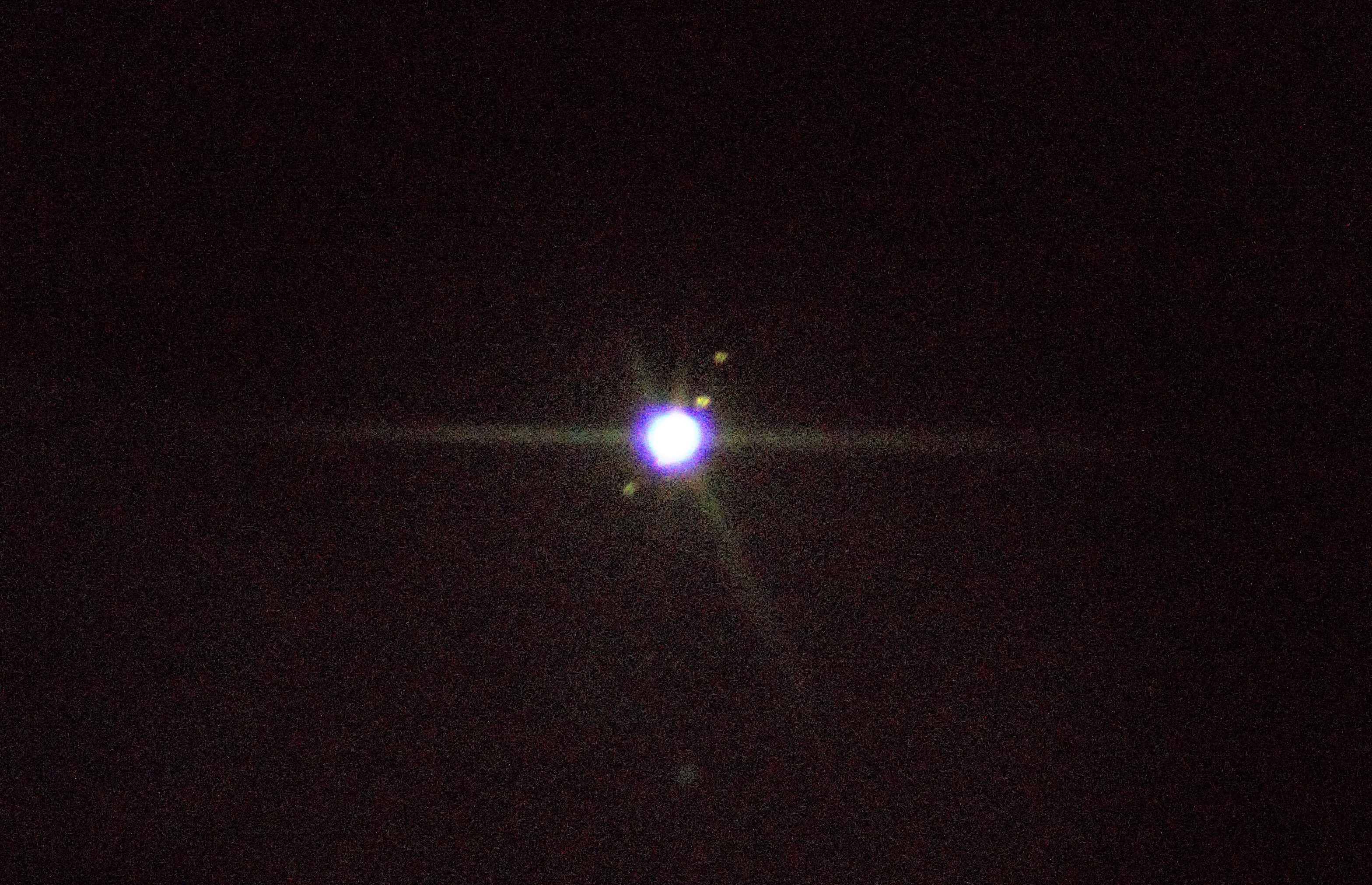 A grainy image of a blue-white dot, being Jupiter, surrounded by 4 moons that appear as blurry dots.